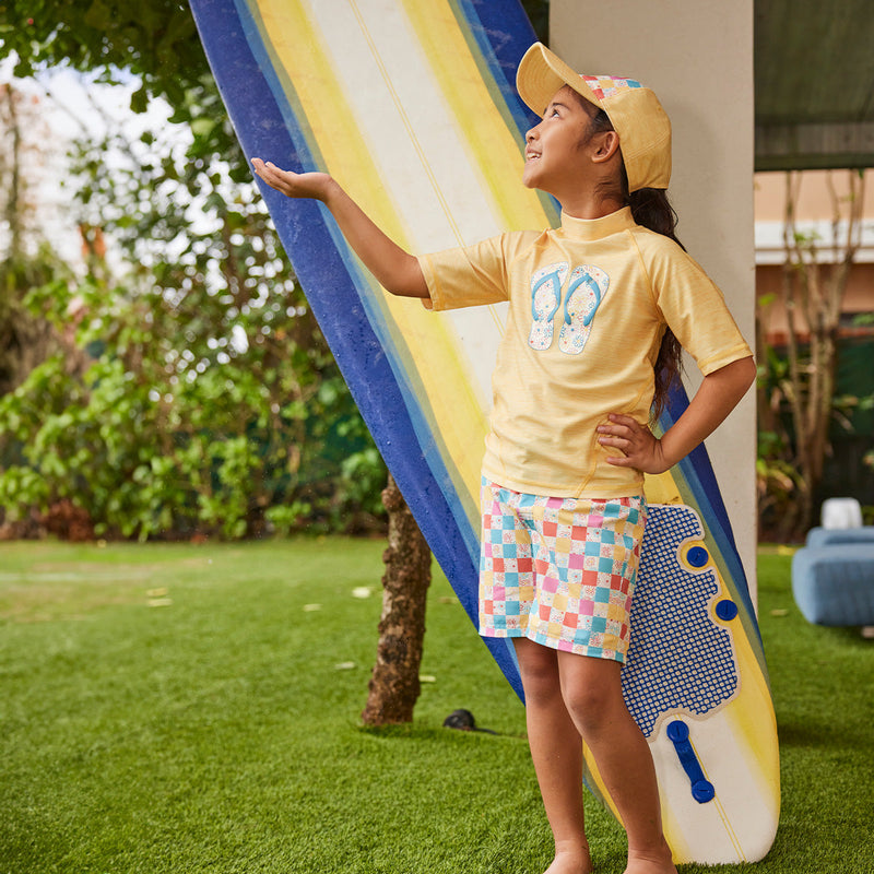 girl by surfboard in board shorts|checkered-daisies